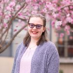 Headshot of Renee Christensen outside in front of a tree with pick flowers 